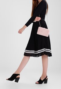 Black pleated skirt with white stripes, paired with open-toe black heeled shoes. A light pink faux fur clutch with chain sits in hand.