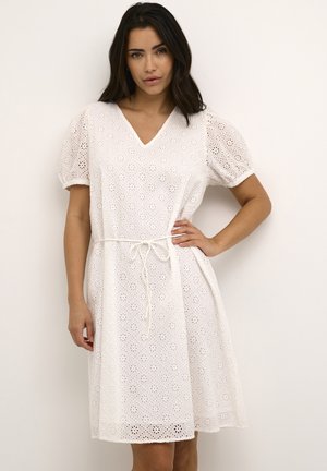 Robe en coton blanc avec un décolleté en V et des manches courtes bouffantes. Présente des motifs en œillets décoratifs et une ceinture à nouer à la taille.