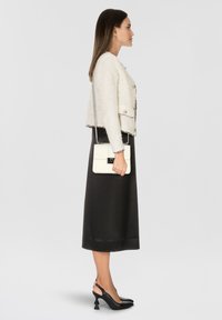 Chaqueta blanca de tweed con cierre de botón plateado, combinada con una falda de satén negra y tacones de slingback negros; sosteniendo un bolso cruzado blanco.