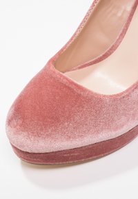 Pompe en velours rose doux, avec un bout carré et une plateforme lisse. La texture est moelleuse avec un éclat subtil sur le matériau.