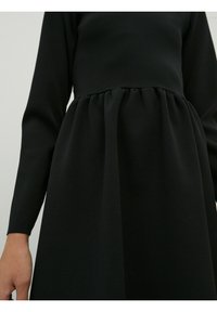 Zwarte gebreide jurk met lange mouwen, met een aansluitend lijfje en een gathered rok. De stof heeft een gladde textuur en een consistente kleur.