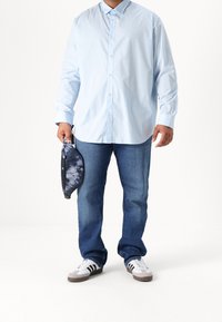 Camicia azzurra con bottoni, jeans di denim, borsa decorata in blu/nero e sneakers bianche con strisce nere. Outfit casual con vestibilità ampia.