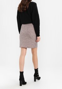 Pull en noir court, jupe rose en tricot côtelé, bottines avec accents de boutons, talons hauts, texture lisse, silhouette ajustée.