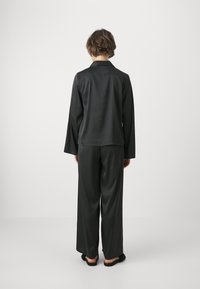 Svart satinpyjamas-set med långärmad topp och vida byxor. Slät textur, enkel krage och avslappnad passform. Badtofflor ingår.