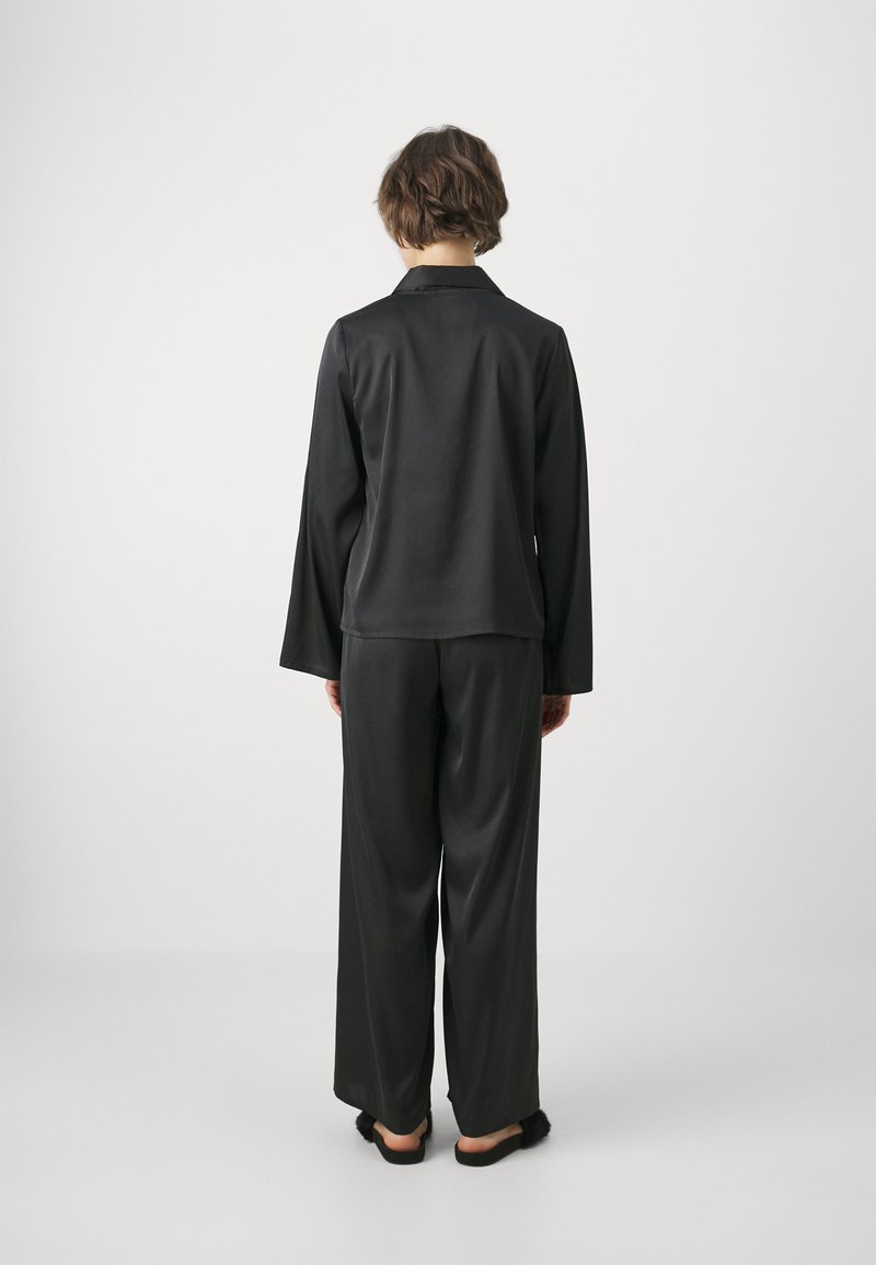 Conjunto de pijama de satén negro que incluye una blusa de manga larga y pantalones de pierna ancha. Textura suave, cuello sencillo y corte relajado. Incluye pantuflas.