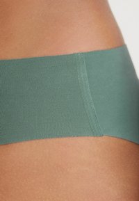 Groene naadloze ondergoed met een gladde, zachte textuur en een laag uitgesneden ontwerp. Bevat een zacht gebogen tailleband en minimale stikseldetails.