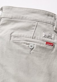 Close-up of light gray Levi's pants back pocket with button closure, Levi Strauss branded patch, and red Levi's fabric tag.