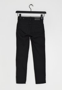 Jeans skinny negros colgados en un perchero, hechos de denim, con una textura suave, dos bolsillos traseros y una etiqueta en la cinturilla.