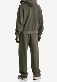 Sudadera con capucha y pantalones a juego en verde oliva apagado, hechos de una suave mezcla de algodón. Presentan un ajuste cómodo y detalle de bolsillo lateral.