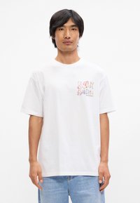 Λευκό βαμβακερό t-shirt με κοντά μανίκια, με πολύχρωμο κείμενο και γραφικό αστέρι στην αριστερή περιοχή του στήθους. Απλός, χαλαρός σχεδιασμός.