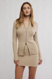 Πλεκτή μπεζ ζακέτα με φερμουάρ μπροστά, ριμπ υφή και εφαρμοστή σιλουέτα. Συνδυασμένη με αντίστοιχο ριμπ κοντό φόρεμα.