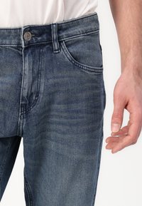 Jeans in denim blu scuro con un finish sbiadito, dotati di chiusura a bottone, cinque tasche e dettagli di cucitura visibili vicino alla vita.