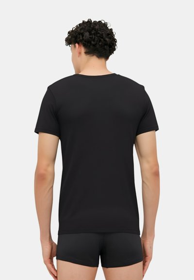T-shirt nera a maniche corte con colletto rotondo, texture liscia e design aderente, vista da dietro, abbinata a pantaloni corti neri.