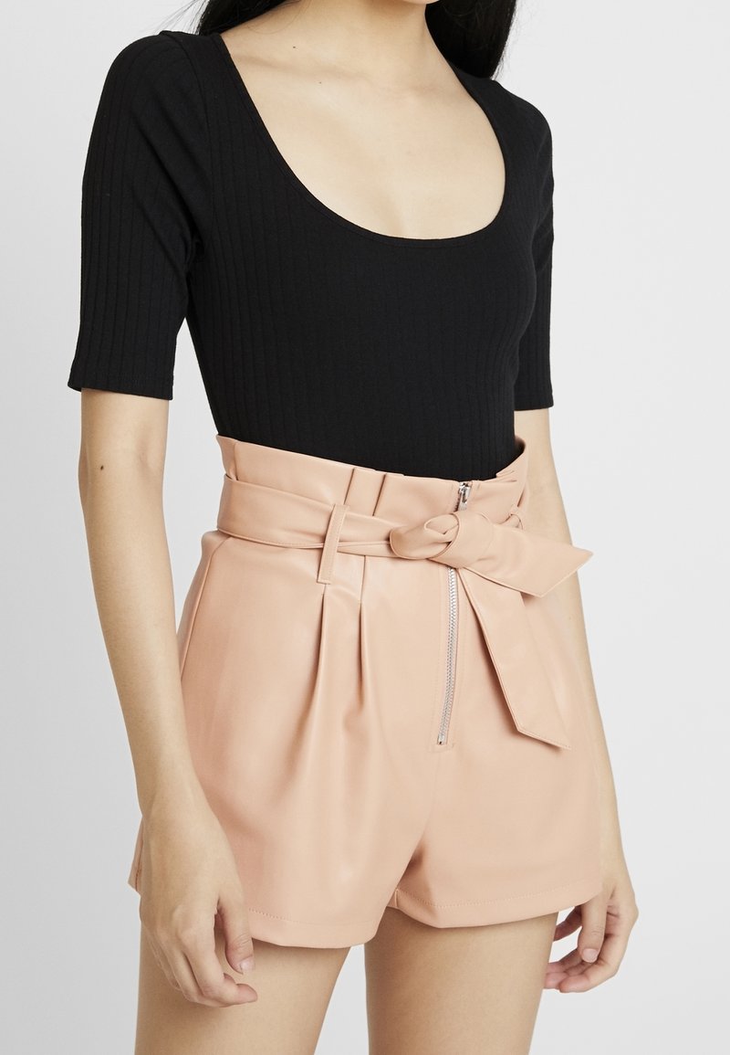 Femme portant un top noir côtelé à encolure dégagée et un short beige taille haute avec fermeture éclair devant et ceinture nouée en nœud.