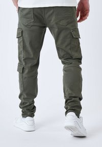 Pantaloni cargo verde oliva, realizzati in cotone. Presentano tasche laterali, dettagli cuciti e gambe affusolate, abbinati a sneakers bianche.