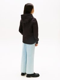 Melna kapuce ar kapuci, apvienota ar gaiši ziliem platiem džinsiem. Melni platformas apavi noslēdz apģērbu. Vienkārša fonu.