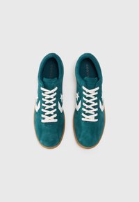 Ténis de camurça turquesa com atacadores brancos, apresentando uma estrela branca e um design em forma de chevron. Sola de borracha em tons de caramelo, textura suave e bico arredondado.