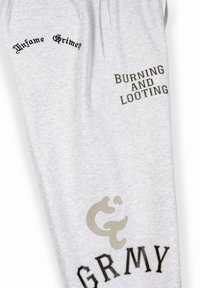 Pantalons de jogging gris avec texte imprimé : "Infame Grimey," "BRÛLAGE ET PILLAGE," et "GRMY." Texture lisse avec un design décontracté.