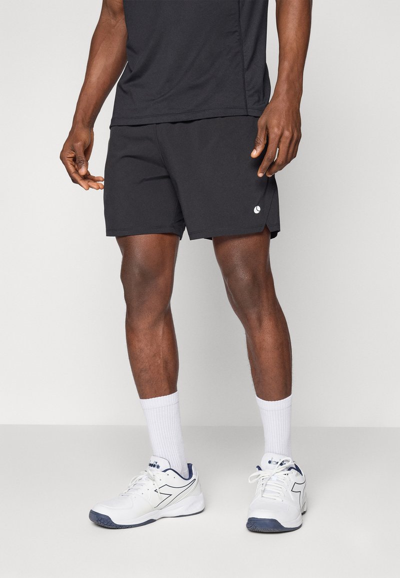 Black athletic shorts with a logo on the bottom hem, paired with white socks and white athletic shoes, worn with a black short-sleeve top.