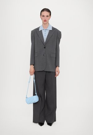 Grauer gestreifter oversized Blazer, hellblaues Hemd mit Kragen, weit geschnittene graue Hosen und eine kleine runde hellblaue Handtasche. Schwarze spitze Schuhe.