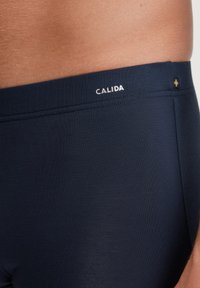 Navy blue swim shorts made of smooth fabric; features a CALIDA logo in white on the waistband and a subtle, clean design.