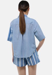 Chemise à manches courtes rayée bleue avec un ourlet arrondi, associée à un short rayé bleu et blanc, fabriqué en tissu léger.