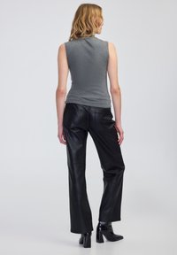 Šedý top bez rukávů s texturovanou tkaninou, kombinovaný s vysokými černými koženými kalhotami a černými kozačkami na podpatku.