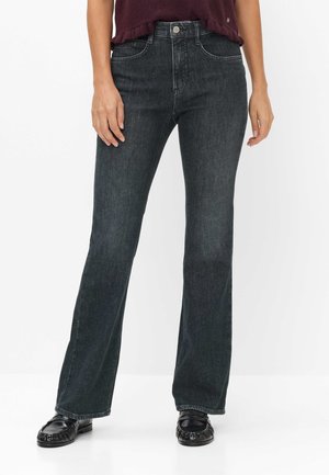 Frau trägt dunkelgraue Bootcut-Jeans, schwarze Loafers und ein kurzärmeliges, dunkelburgunderfarbenes Oberteil, das an der Taille abgeschnitten ist.