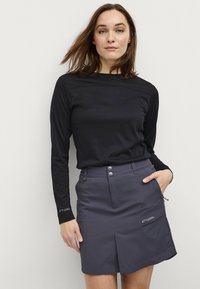 Zwarte langemouwen shirt met ronde hals, gecombineerd met een grijze rok tot de knie met twee voorkruiszakken en drie metalen knopen.