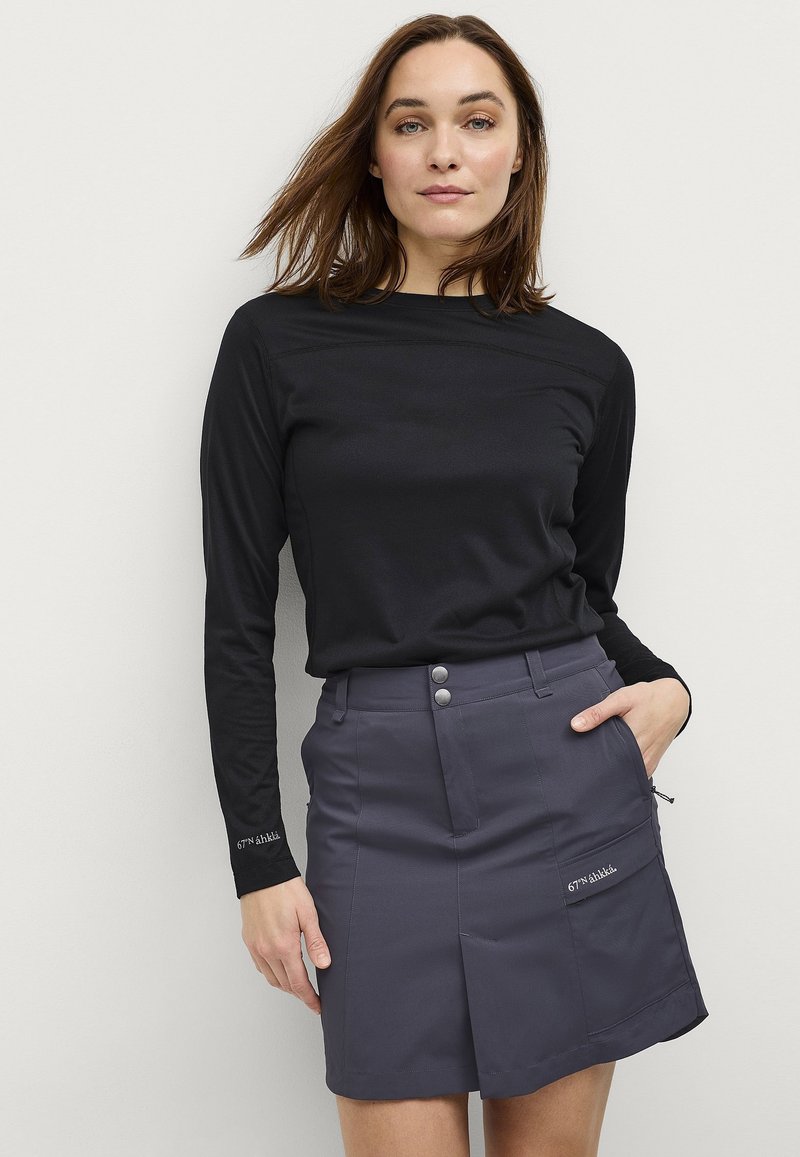 Zwarte langemouwen shirt met ronde hals, gecombineerd met een grijze rok tot de knie met twee voorkruiszakken en drie metalen knopen.