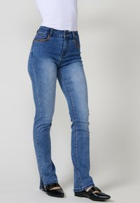 Siniset farkut, joissa on kapea malli, koristeompeleita taskuissa ja sivureikä helmoissa. Yhdistetty mustiin ballerinoihin.