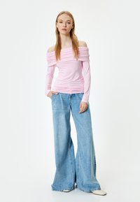Helltauzes Carmen-Top mit Raffung, kombiniert mit weiten blauen Jeans. Das Outfit hat lange Ärmel und eine figurbetonte Silhouette.