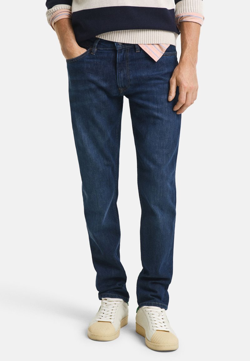 Jeans in denim blu scuro con vestibilità dritta, design a cinque tasche e una texture liscia. Indossati con sneakers bianche.