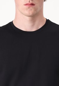 Juoda medvilninė marškinėliai su apvalia iškirpte ir trumpomis rankovėmis; lygi tekstūra su minimaliu dekoravimu.