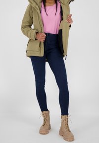 Veste rembourrée vert olive, t-shirt rose, jeans skinny bleu foncé et bottines beige à lacets avec des semelles épaisses.
