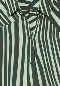 Camicia button-up con strisce verticali nere e bianche su uno sfondo verde. Realizzata in tessuto morbido, dotata di colletto classico e bottoni davanti.