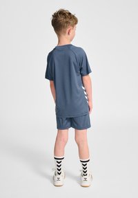 Niebieski zestaw sportowy składający się z krótkiego rękawa i szortów, wykonany z gładkiego materiału. Białe paski po bokach, do tego skarpetki z wzorem.