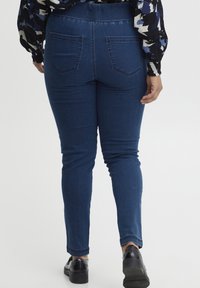 Jeans skinny azul oscuro con cintura alta, textura de denim suave y dos bolsillos traseros. Combinados con zapatos negros y una blusa estampada.