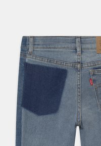 Jeans dżinsowe w średnim niebieskim odcieniu, z ciemnoniebieską kieszenią naszytą. Klasyczny pięciokieszeniowy fason z pomarańczowymi szwami i etykietą logo z tyłu.