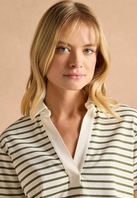 Valge ja rohelise triibulise kujundusega särk, valmistatud pehmest kangast, millel on krae ja V-kaelus. Lihtne disain, millel on vahelduvad triibud.