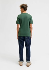 Groene T-shirt met korte mouwen, gemaakt van zachte stof, gecombineerd met donkerblauwe spijkerbroek met opgerolde mouwen. Lichtgekleurde robuuste schoenen maken de look compleet.