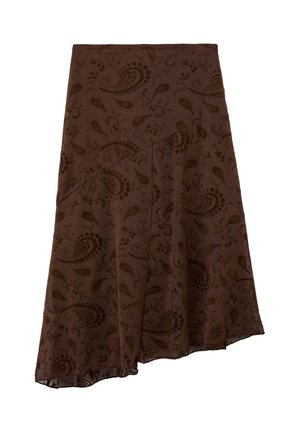 Jeune femme vêtue d'un top court noir, d'une veste en cuir noire, d'une jupe marron à motifs et de bottes noires montant jusqu'aux genoux, debout devant un fond blanc.