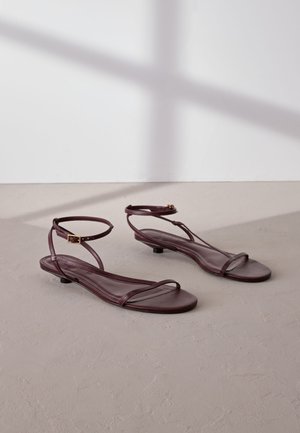 Sandalias planas de cuero burdeos con dos tiras delgadas y una correa ajustable en el tobillo, con un pequeño tacón y una textura suave.