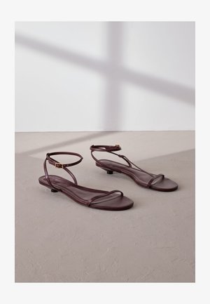 Płaskie sandały z bordo skóry z dwoma cienkimi paskami oraz regulowanym paskiem wokół kostki, wyposażone w niewielki obcas i gładką fakturę.