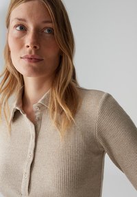 Beige ribgebreide trui met een kraag met knopen en lange mouwen, voorzien van een textuurafwerking en subtiele verticale strepen.