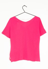T-shirt rosa a maniche corte, realizzata in tessuto leggero, con scollatura a V e spacchi laterali sull'orlo, appesa a un gancio nero.