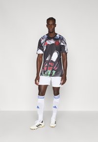 Maglia da calcio nera con motivi colorati, collo rotondo, logo rosso. Pantaloncini e calze bianchi con strisce blu. Scarpe da calcio bianche con accenti neri.
