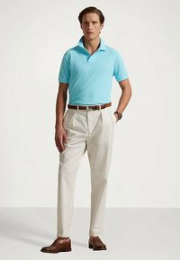 Lys blå poloskjorte med klassisk krage, kombinert med kremfargede bukser. Brunt belte og sko i skinn fullfører antrekket. Enkel, elegant design.