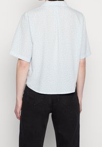 Light blue short-sleeve shirt with a floral pattern, collar, and a curved hem; made of a soft, lightweight fabric.