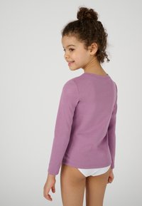 Camicia a maniche lunghe in cotone lavanda chiaro, con scollo rotondo e design aderente, mostrata da dietro con una texture liscia.